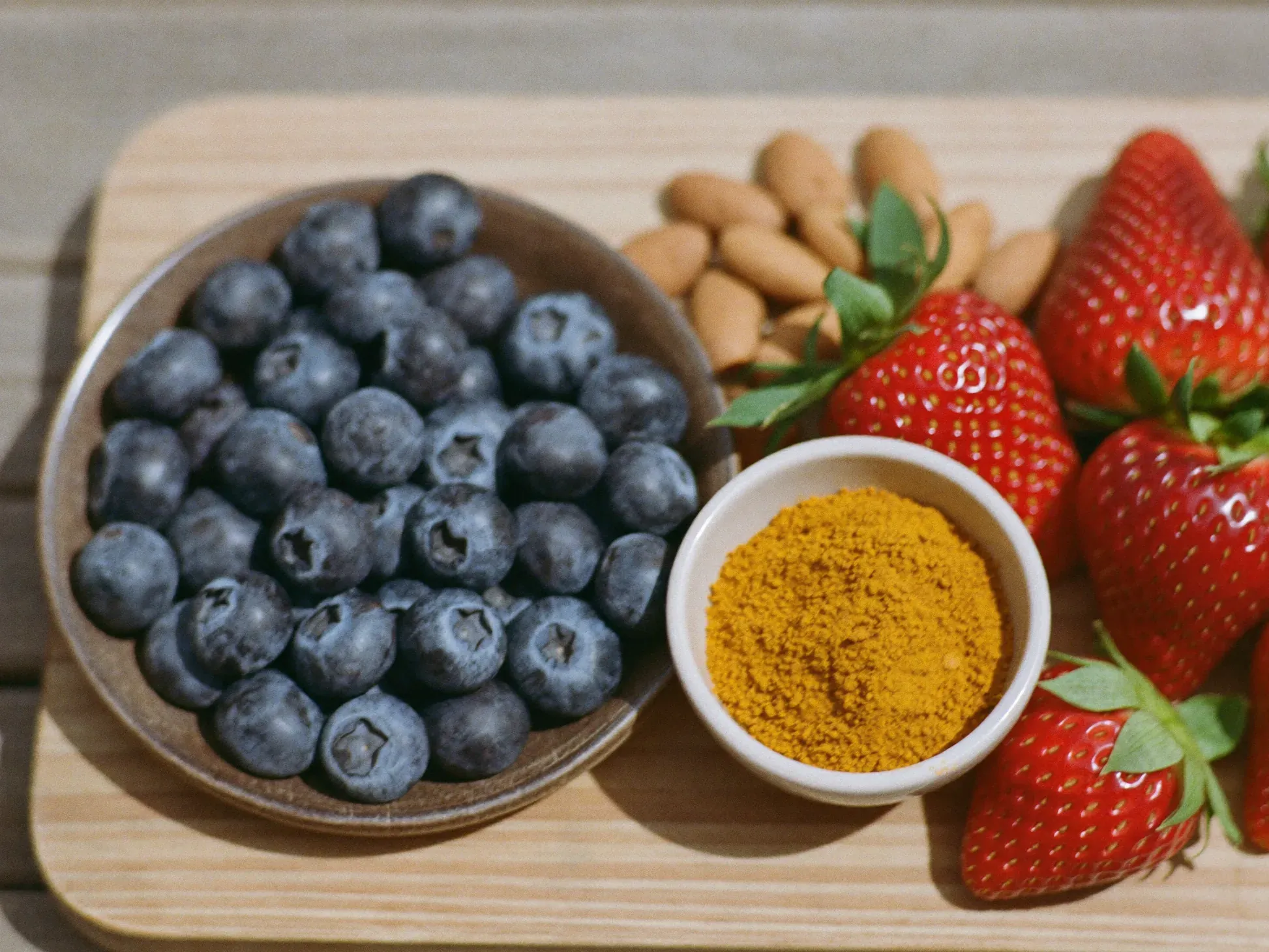 http://Tabla%20de%20madera%20con%20arándanos,%20frutillas,%20almendras,%20nueces%20y%20un%20cuenco%20de%20cúrcuma.