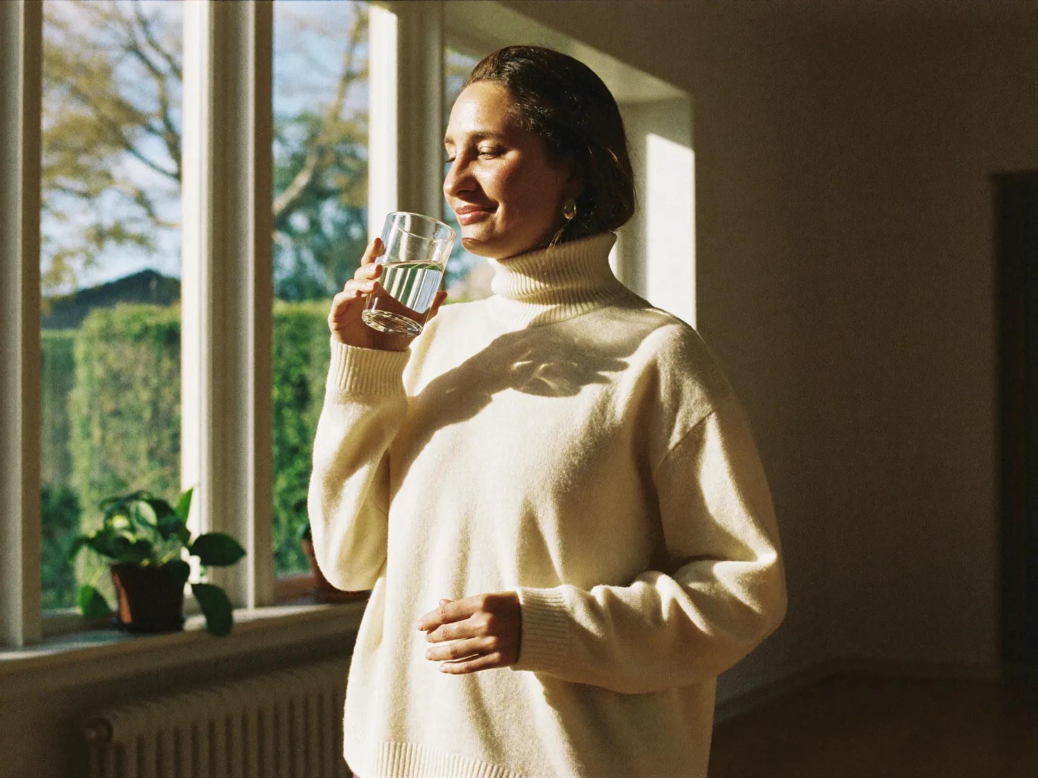 http://Mujer%20bebiendo%20un%20vaso%20de%20agua%20junto%20a%20la%20ventana,%20con%20luz%20natural%20de%20la%20mañana.